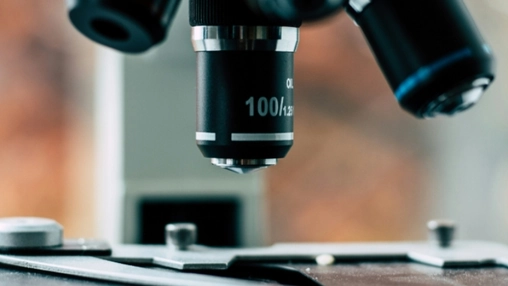 Close-up of a black 100x microscope objective lens above glass slides on a laboratory microscope stage
